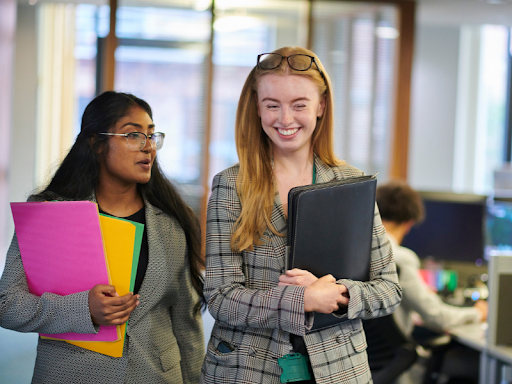 two female smiling holding files and folders